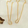 Pavé Horseshoe Pendant Necklace product image 2 Two gold-tone pavé horseshoe necklaces arranged on warm ivory fabric