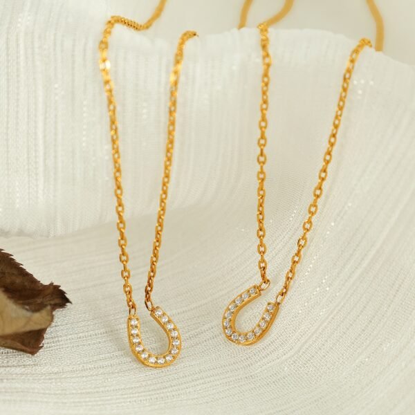 Pavé Horseshoe Pendant Necklace product image 2 Two gold-tone pavé horseshoe necklaces arranged on warm ivory fabric