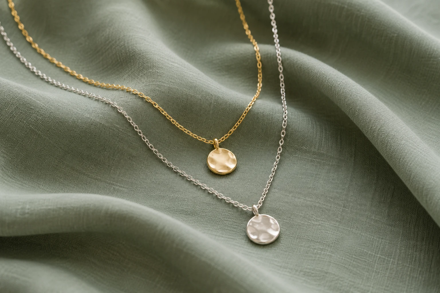 Gold-tone and silver-tone necklaces arranged on soft sage fabric